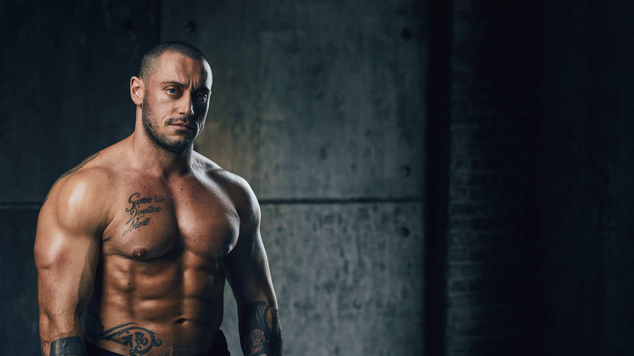Gianluca Mazzolini, personal trainer a Brescia, a torso nudo in una palestra dalle pareti in cemento